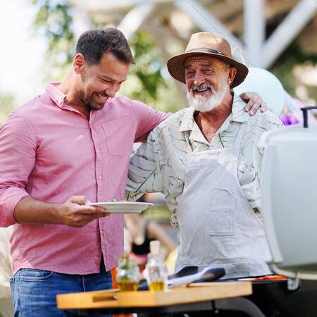 Adult son standing with his arm around his father beside a grill at a barbecue