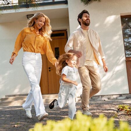 Family of three walks in front of their home smiling and holding hands