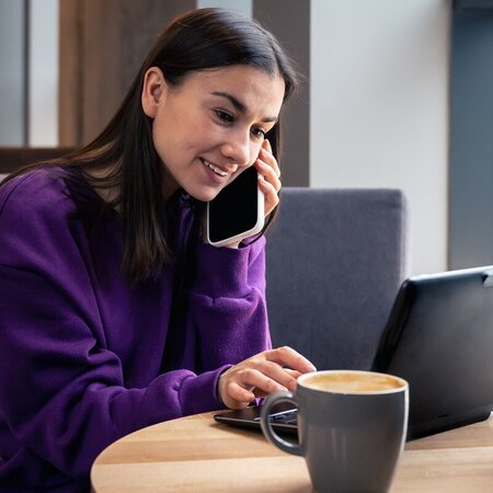Woman speaking with customer support on her cell phone while reviewing a website on her laptop