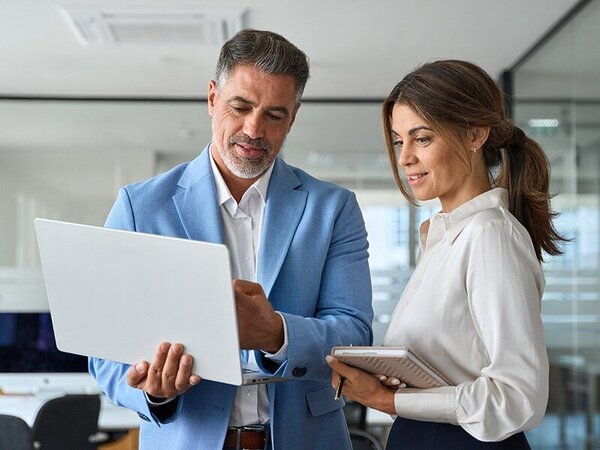 Two business professionals reviewing a laptop together in a corporate office