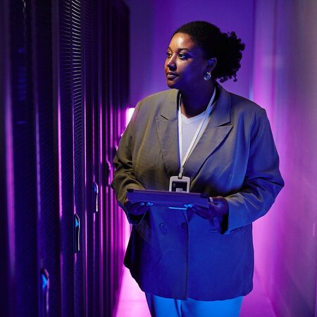 A woman in a blazer holding a tablet beside data center servers